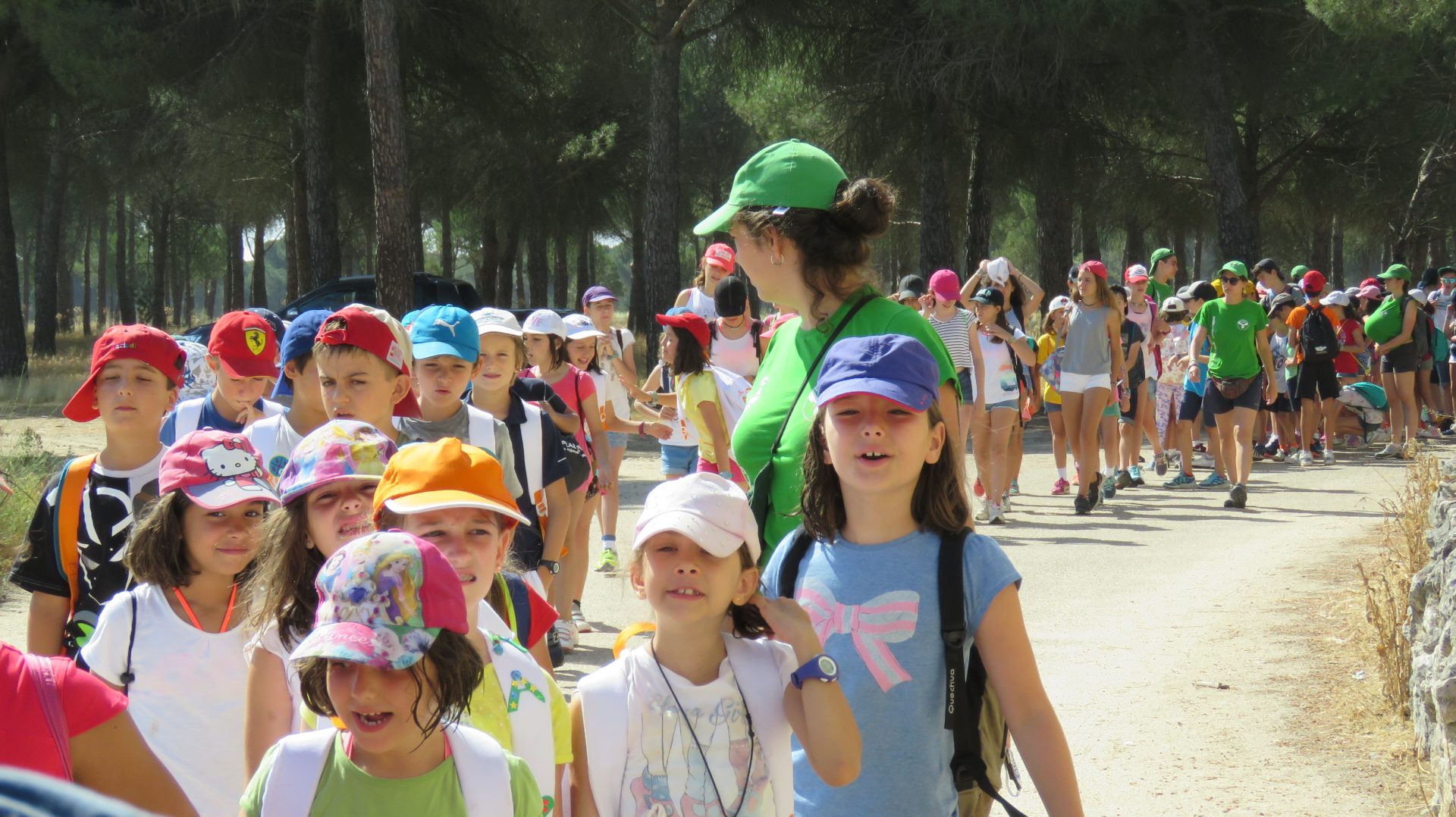 Un grupo de niños caminando juntos en un día soleado, sonriendo y charlando mientras disfrutan de su tiempo al aire libre.