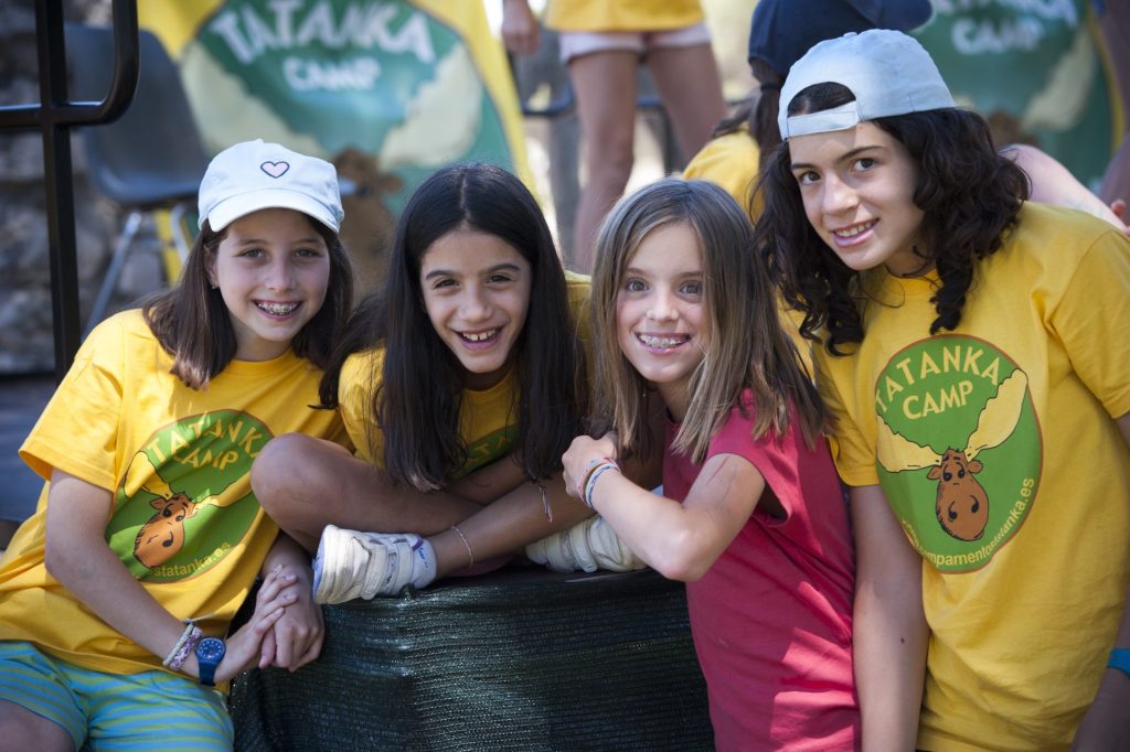 Cuatro chicas con camisetas amarillas sonriendo y posando juntas para una foto de grupo.