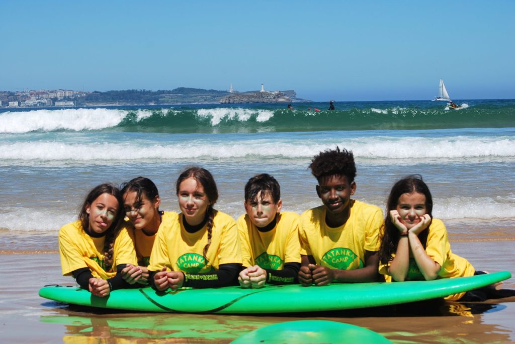 Un grupo de cinco personas haciendo equilibrio sobre una gran tabla de surf, disfru- tando de un dia coleado en la nlava.